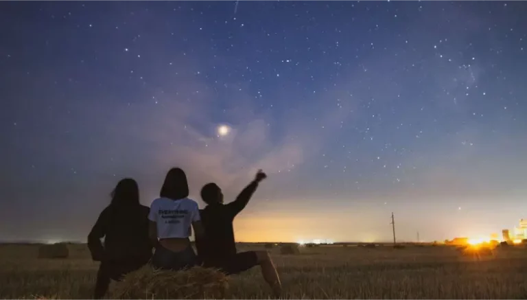 Deux filles et un garçon qui sont assis sur l'herbe et contemple les étoiles